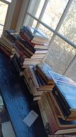 Stacked books on a dark wood surface near a window, showing a large collection of historical books.