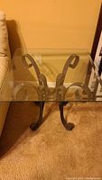 Front angle photo showing glass top and curled iron base of an end table next to a beige sofa.