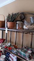 Shelf with ceramic pieces, glass shell display, and handcrafted candles organized along with cloth basket and napkins.