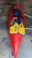 Full view of a red single-person kayak with life vest and gear on top.