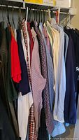 View of various men's shirts hanging in closet, various colors and patterns including button-up and polo styles.