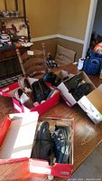 Overview of five pairs of men's shoes in boxes on table including work sneakers, loafers and dress shoes