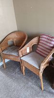 Front view of two natural rattan chairs with cushions on carpeted floor.