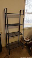 Front view of the charcoal metal shelving unit showing four metal slat shelves and a rectangular frame.