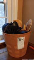 Large ceramic pot filled with various kitchen utensils including black ladles, spatulas, and wooden spoons near a window.