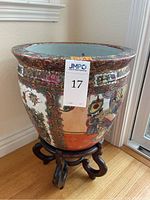 Side view of large ceramic fishbowl planter on carved wooden stand showing painted Chinese figures and decorative patterns.