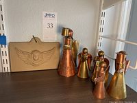Front view of copper and brass angel figurines and wall hanging plaque arranged on a shelf.