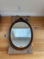 Full view of the oval mirror with wooden frame laid on cardboard, showing overall shape, size, and frame condition.