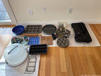 Overview photo showing all items together including blue ceramic bowl, pans, cookie stamps, cutters, baking cups, molds, rolling pin, cake saver, hot pads and electric griddle.