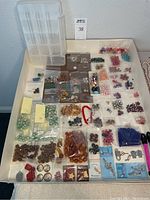 Wide view of assortment of beads in plastic bags, charms, and organizer on a table.