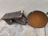 Redwood bench and two rusted steel disks on concrete surface, showing weathering and condition