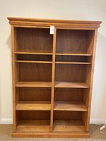 Front view of the wooden bookcase showing two columns of shelves divided by a central vertical panel with crown molding on top.