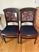 Front view of both chairs showing carved crest rails, needlepoint backs and upholstered seats