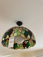 View of the stained glass lamp mounted on the ceiling with grapevine design and a visible crack in one piece of glass.