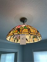 Ceiling lamp hanging, showing pink flowers stained glass pattern from side angle with ceiling fixture and metal chain.