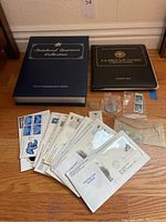 Overview photo of the lot showing Statehood Quarters Collection binder, U.S. First Day Covers book, multiple first day cover envelopes, loose stamps, and coins.
