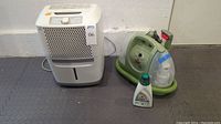 Frigidaire dehumidifier and Bissell Little Green carpet cleaner placed side by side on gray floor.