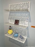 Full view of three white enameled perforated metal shelves mounted on wall with decorative items arranged on them.