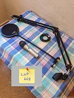 Microphone with desk arm, pop filter, USB cable on blue plaid surface, yellow note with lot number visible