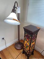 Shows both lamps together, highlighting the adjustable brushed copper lamp with white glass shade and the stained glass pedestal lamp