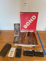Overhead view of drafting and calligraphy tools including curve-making instruments, rulers, pens, nib boxes, Art Bond pad, and row of three Hewlett-Packard calculators.