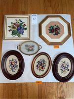 Top-down photo of all five framed needlepoint pieces showcasing floral designs and frame styles.