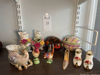 Shelf display showing multiple porcelain and decorative items including lidded boxes, Royal Albert shoes, bird salt and pepper shakers, kitty creamer, seashell bowl, and gold mule figurine.