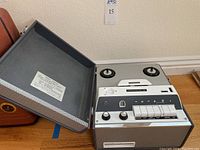 Open reel-to-reel tape player showing control panel, speaker grill, and reel spindles.