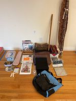 Photo showing wide view of assorted sewing and craft supplies including fabric remnants, folded and rolled fabrics, needle lace books, small tools and notions, sleeve ironing board, and scrapbooking supplies.