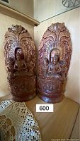 Pair of hand carved wooden Buddha statues shown from front right angle in corner with doily nearby