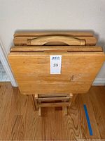 Four beechwood TV trays stacked vertically in a stand showing the top surfaces and handles with visible scratches and water marks.