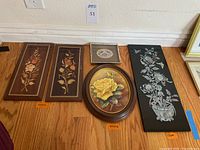 Front view of all five wall art pieces on a hardwood floor showing the oval oil painting, two floral inlaid wood panels, large black panel with mother of pearl inlay, and a small framed jacquard woven floral picture.