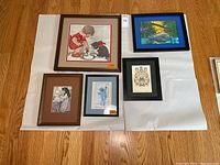 Top view showing all 5 framed artworks laid out on the floor, emphasizing the needlepoint artwork and Disney Jungle Book print with surrounding smaller art pieces.