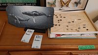 Photo showing painted slate piece with whale art, black stand, and adjacent rock and mineral map on wooden dresser.