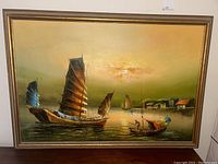 Full view of framed oil painting showing sailboats on calm water at sunset with buildings on the shore in the background.