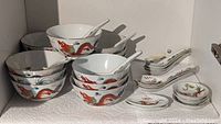 Porcelain bowls with red dragon design stacked along with matching porcelain spoons.