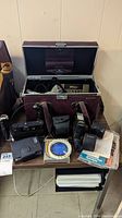 Overall view of burgundy hard camera case open showing assorted cameras and accessories on table