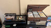 Sony Blu-ray player stacked with DVDs and a large leather-style case filled with cassette tapes on top of a Sony cassette player.
