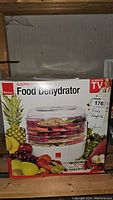 Photo of the Ronco Electric 5 Tray Food Dehydrator in its original box showing colorful fruit graphics and product details on front of box.