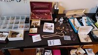 Full assortment of jewellery items spread on a table including earrings, bracelets, necklaces, and brooches in boxes and loose.