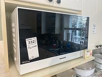 Front view of the Panasonic microwave showing the brand and type on the glass door with the lot tag attached.