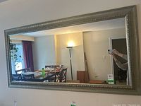 Front view of large rectangular mirror hung on a wall with reflection of a dining area with table, chairs, and lamp