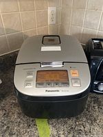 Panasonic SR-ZX105 rice cooker closed on countertop with digital display and controls visible, next to black two-slice toaster.