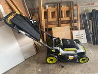 Left side view of Ryobi cordless push lawn mower showing deck, wheels, handle and grass collection bag