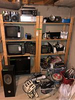 Two tall wood shelving units filled and surrounded by miscellaneous electronics and hardware. Units have natural wood finish and vertical supports with slatted shelves.