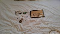 Photo showing assorted jewelry laid flat including brooches, a green insect-shaped pin, a small coin charm, and a boxed pearl necklace set