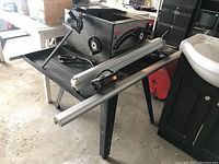 Table saw on stand, showing the saw body, legs of the stand, and aluminum fence rails laid out in front.