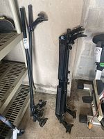 Two Thule roof racks leaning against a wall on a concrete floor, showing overall shape and structure with mounting hardware included.