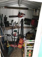 Interior overview showing rotary tiller, chain saw on wall, hedge trimmer, garden supply bags and aluminum chairs