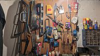 Wide view of pegboard loaded with various hand tools including saws, levels, pliers, staple gun, screws, and hardware items.